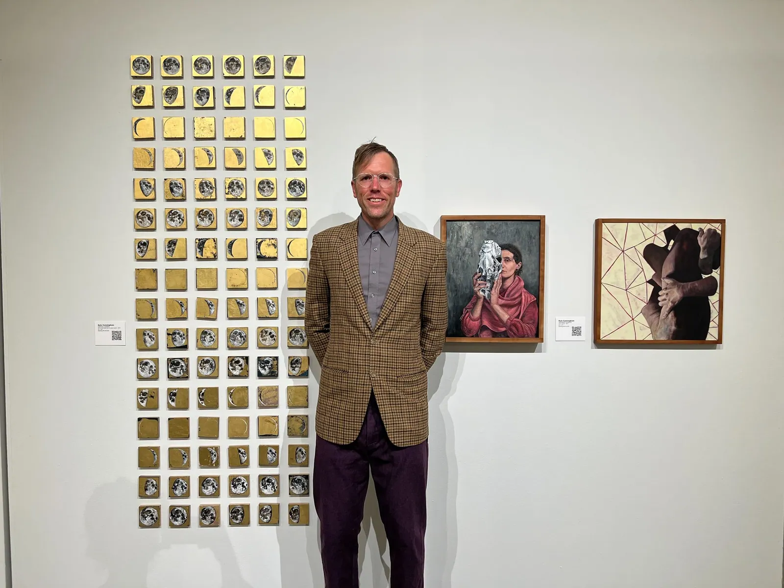 A man stands in front of a wall with paintings on it.