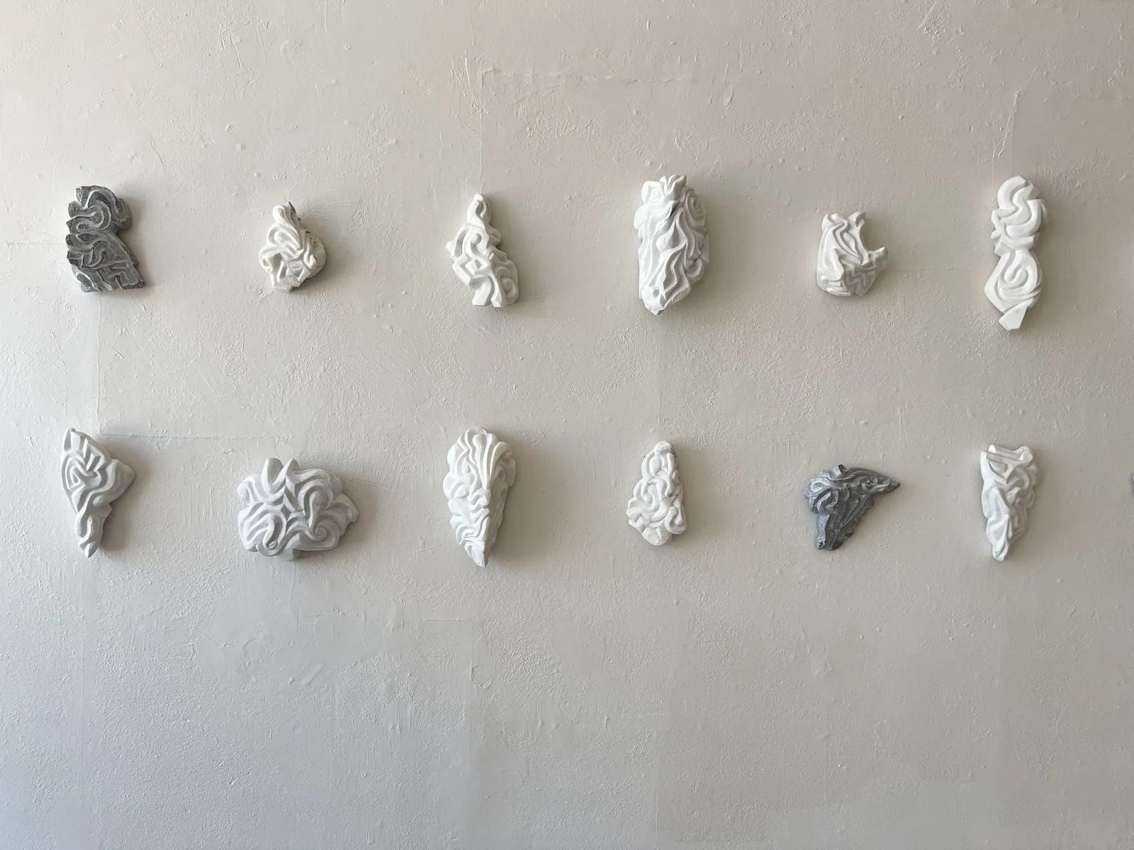 A group of 12 stone carvings mounted to a wall.
