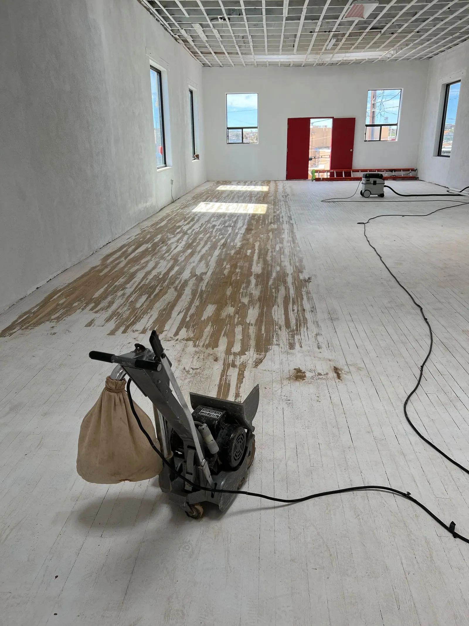 A floor drum sander sits ready to do good work on a white painted wooden floor.
