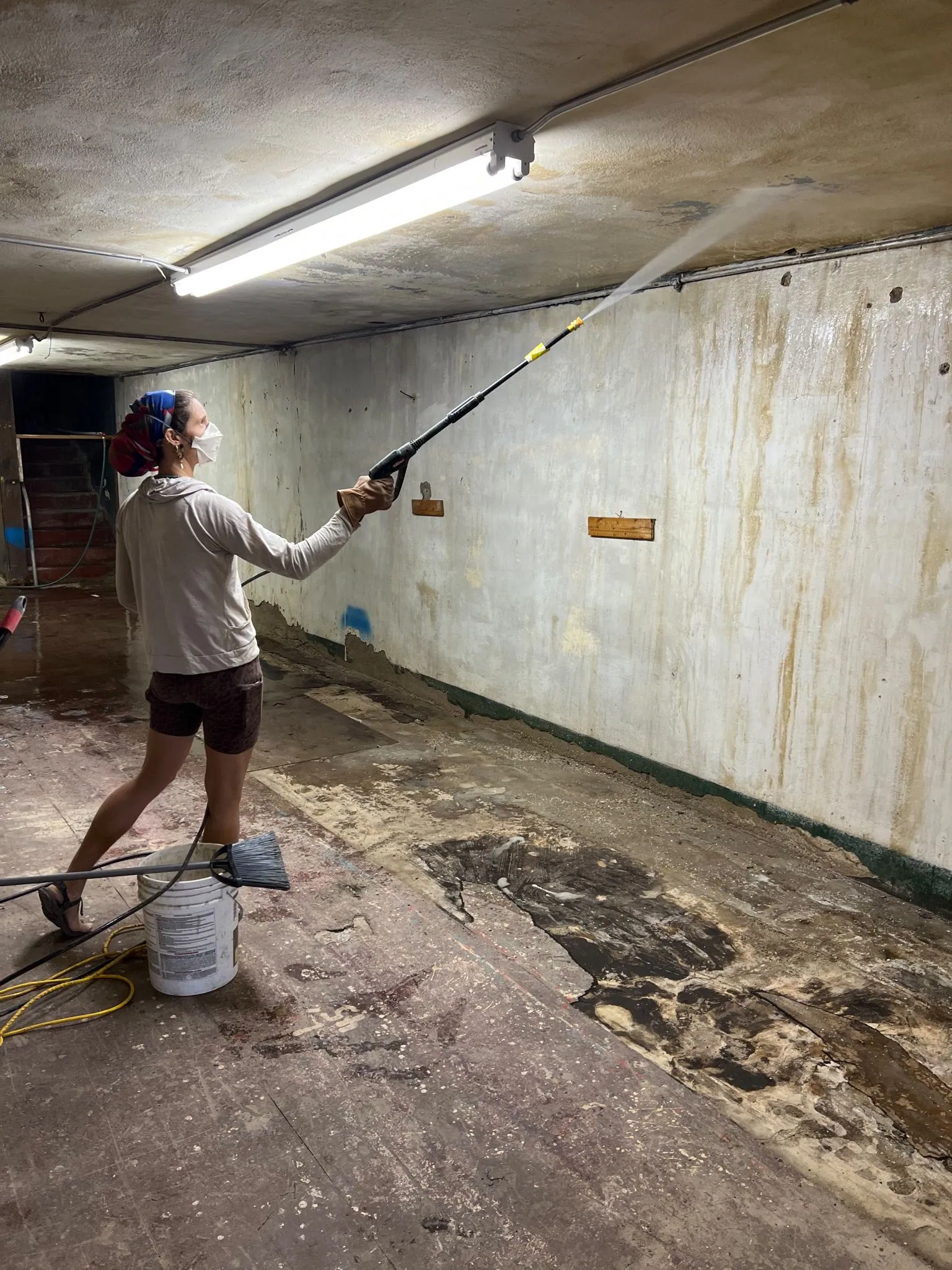 A woman stands in an empty room pressure washing the ceiling.