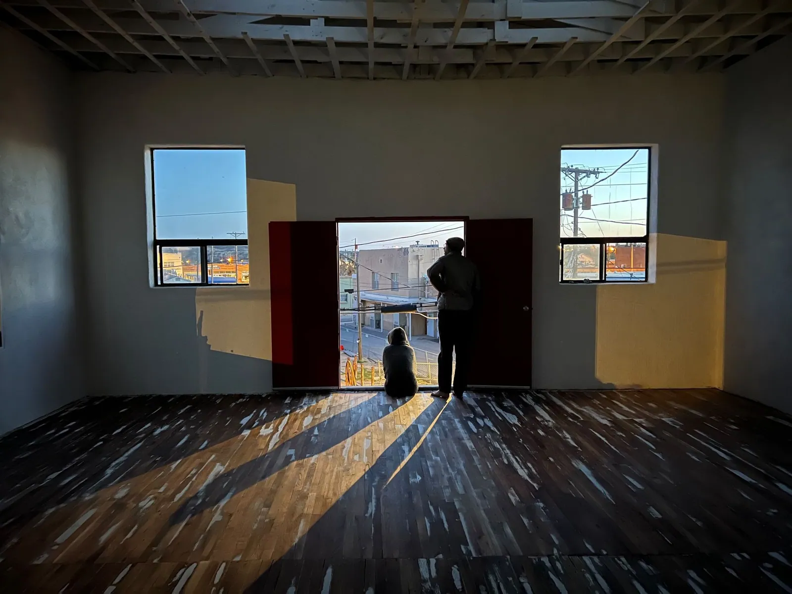 Two people one sitting and one standing in a door way at sunset overlooking a town.