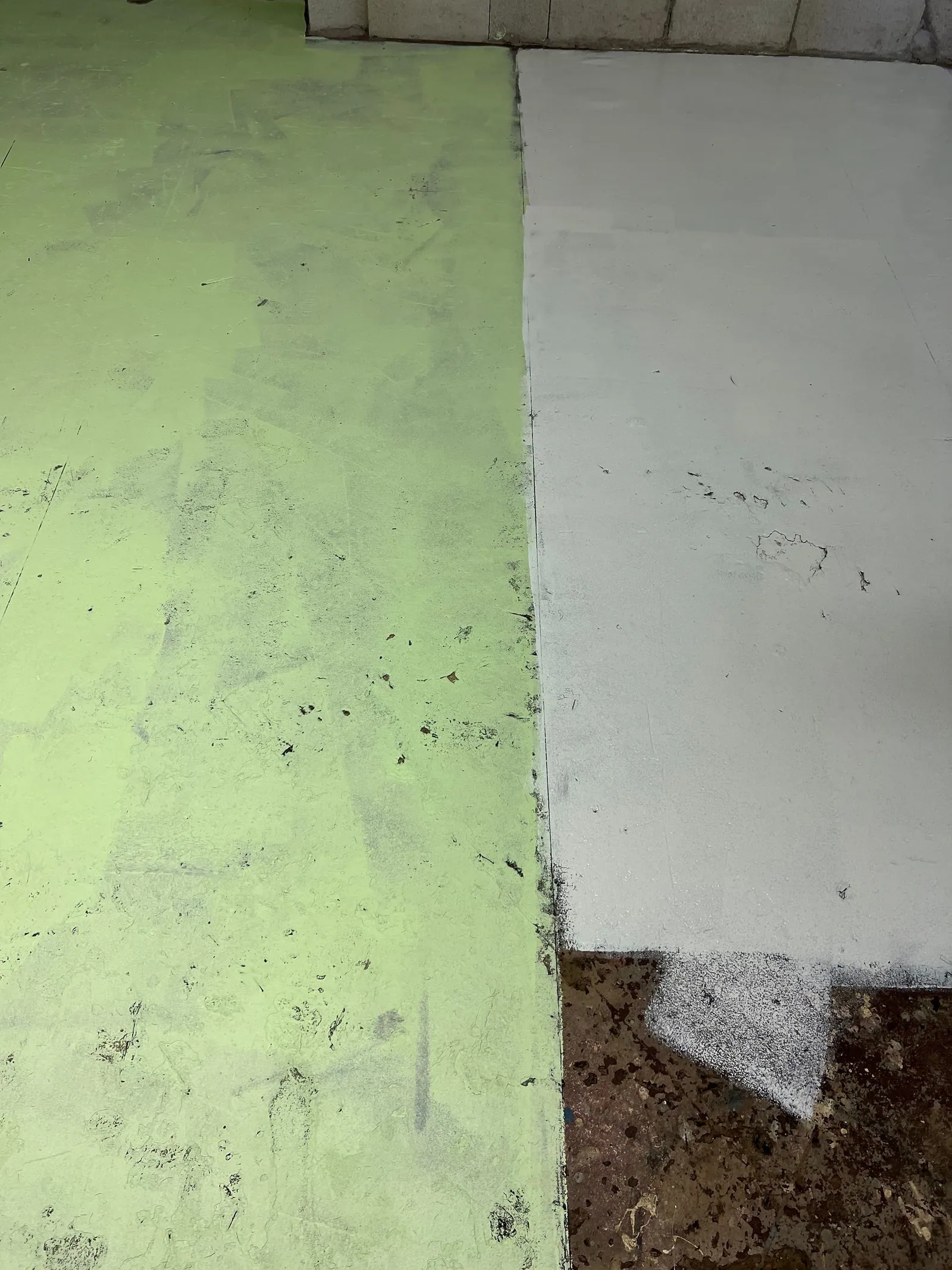 A floor primed with white paint on the right and painted green on the left.