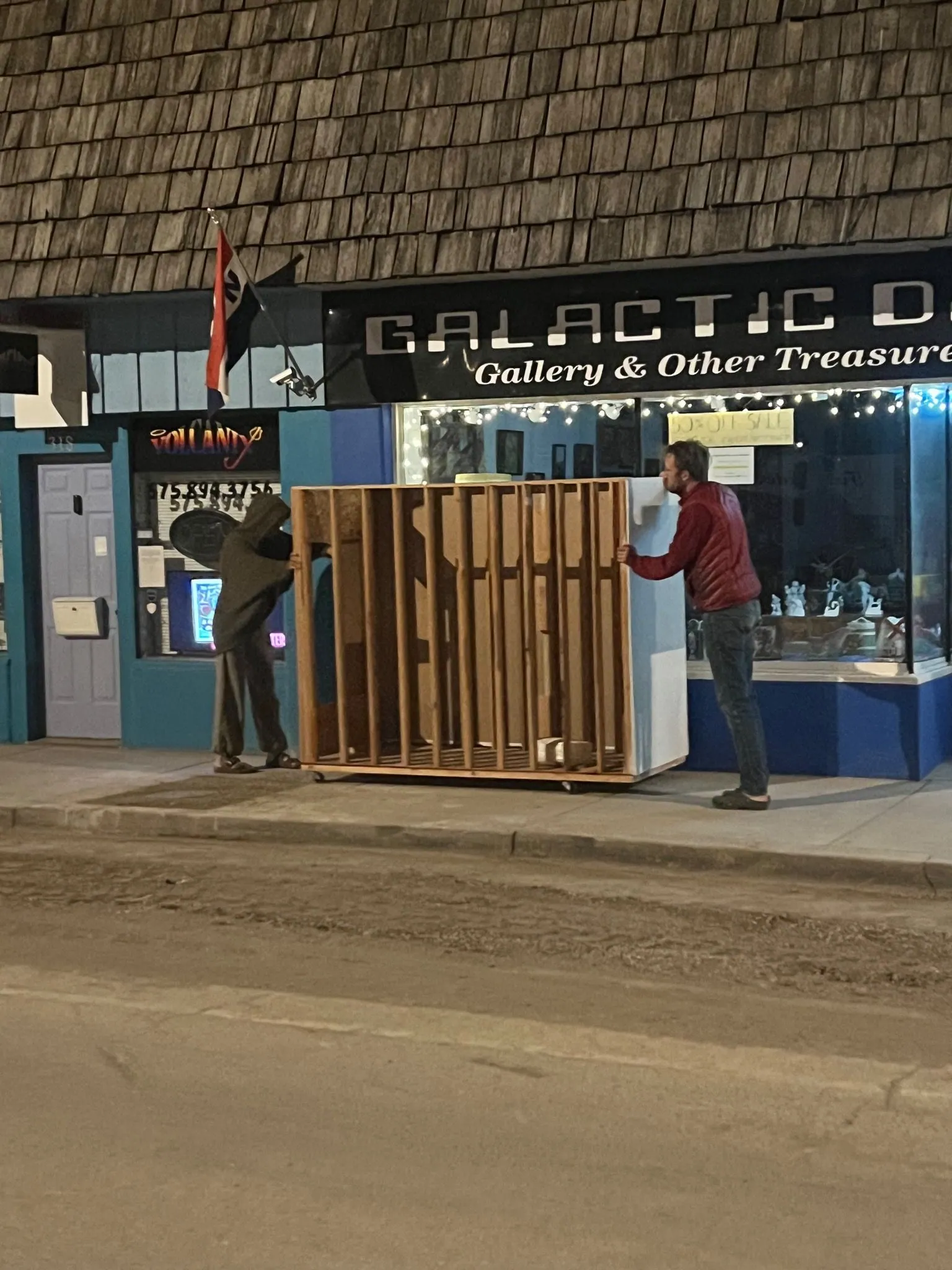 Two people push a painting rack down a sidewalk.