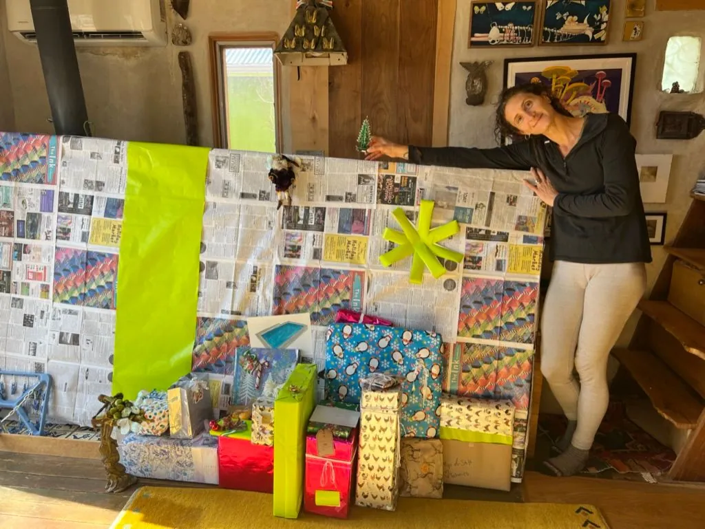 A woman stands in a small room next to a giant present.