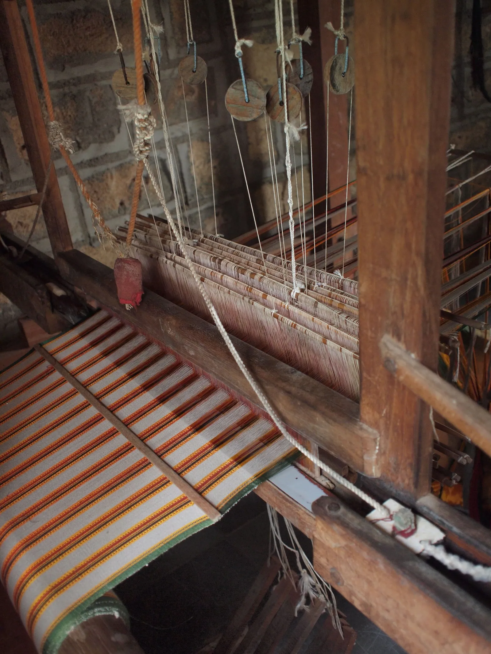 a close up image of a wooden loom with white, red, yellow and green striped fabric on it.