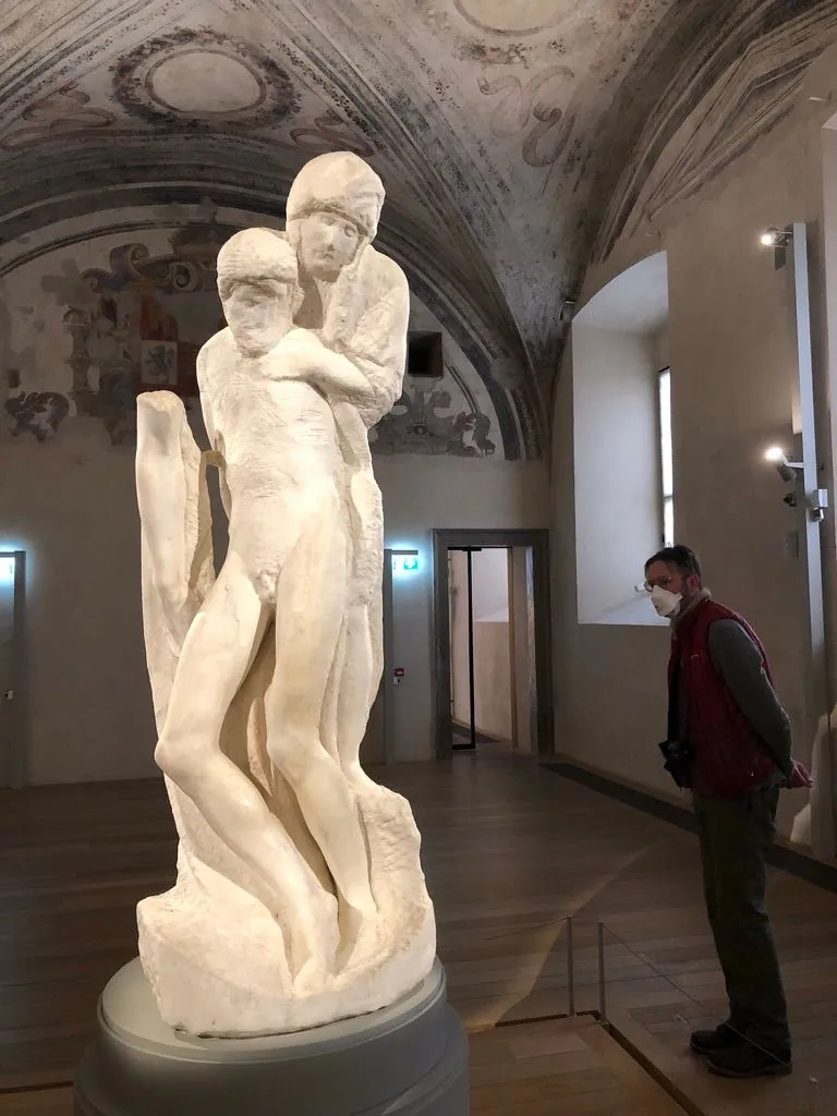A man stares at the back of stone sculpture of a month holding from the back and above her dead limp son.