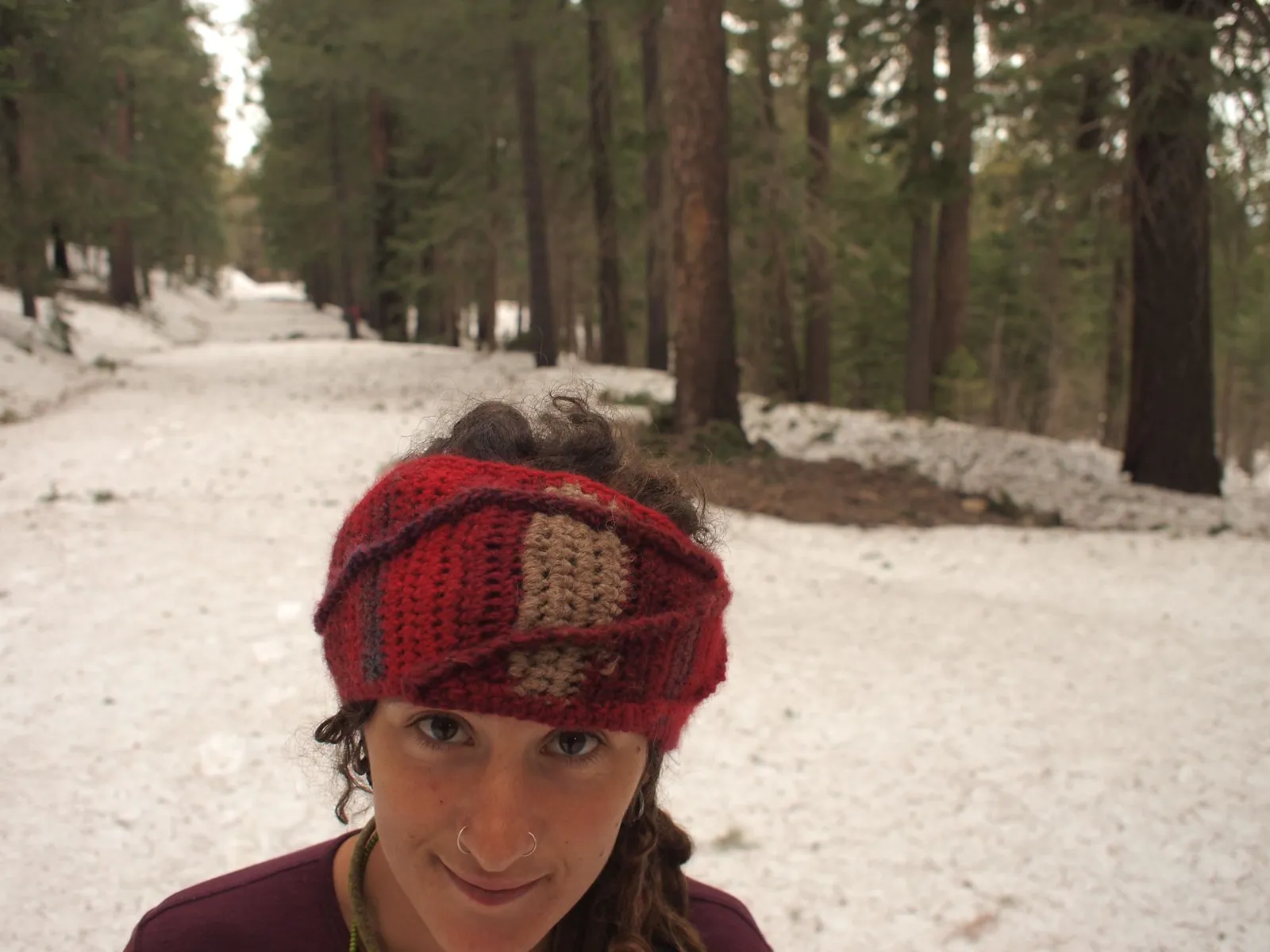 Woman looking at the camera, wearing a red and brown headband, standing in a snowy forest.