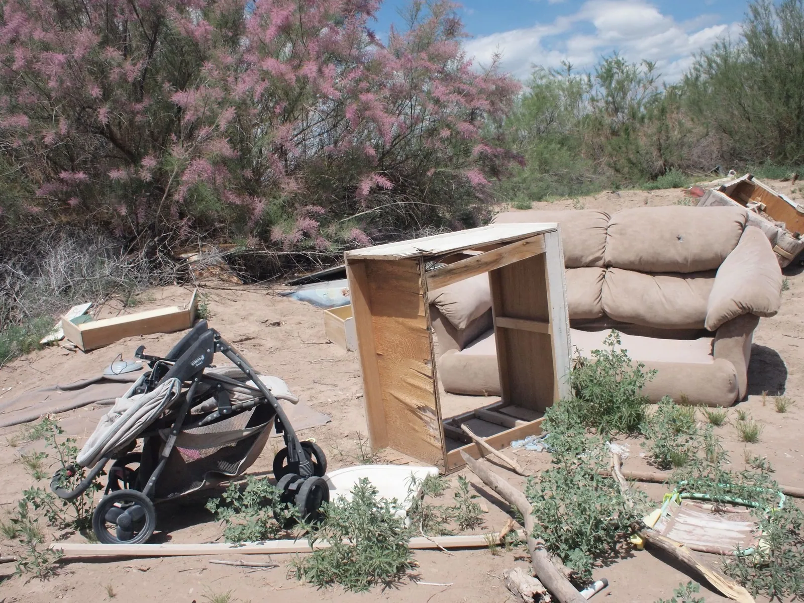 a stroller, destroyed shelving and couch sit in the desert sand